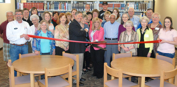 WITH THE CLIP OF THE SCISSORS, officials with Missouri State University-West Plains, the Garnett Library and the Friends of the Garnett Library officially opened the library’s new compact shelving section during a ribbon cutting ceremony hosted by the West Plains Area Chamber of Commerce.  Thanks to Friends’ fund-raising efforts, university officials recently replaced a section of regular shelving with the modern system of shelving for more efficient storage and easy access to reference, periodical and archival materials.  Installation of the mobile compact shelving is the first phase of changing the library from a storehouse of information to a place of access and interaction, university officials said.  Above, Chancellor Drew Bennett and Director of Library Services Sylvia Kuhlmeier prepare to cut the ribbon, which is being held by Chamber Ambassadors Tom Smith, left, and Mallory Prewett.  Behind are university officials, members of the Friends of the Garnett Library and other Chamber Ambassadors.  (Photo provided courtesy of the West Plains Daily Quill)