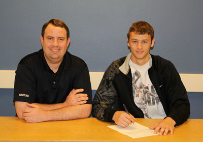 FRESHMAN GRIZZLY BASKETBALL player Desmond Buerge, right, of Carthage, Mo., recently signed a national letter of intent to complete his collegiate playing career at Cameron University in Lawton, Okla. Joining him as he signs his paperwork is Missouri State University-West Plains Grizzly Basketball Head Coach Yancey Walker. (Missouri State-West Plains Photo)