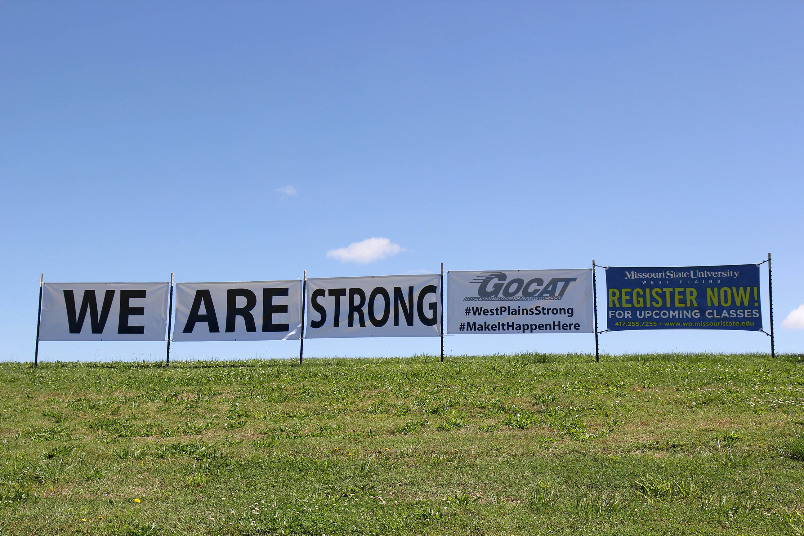 WE ARE STRONG – Officials with the Greater Ozarks Center for Advanced Technology (GOCAT) are showing their resilience with these banners along Broadway near the facility on Howell Avenue in West Plains. Despite devastating flooding in April, training programs offered at the facility will be up and running in time for the fall semester, which begins Aug. 21, they said. (Missouri State-West Plains Photo)