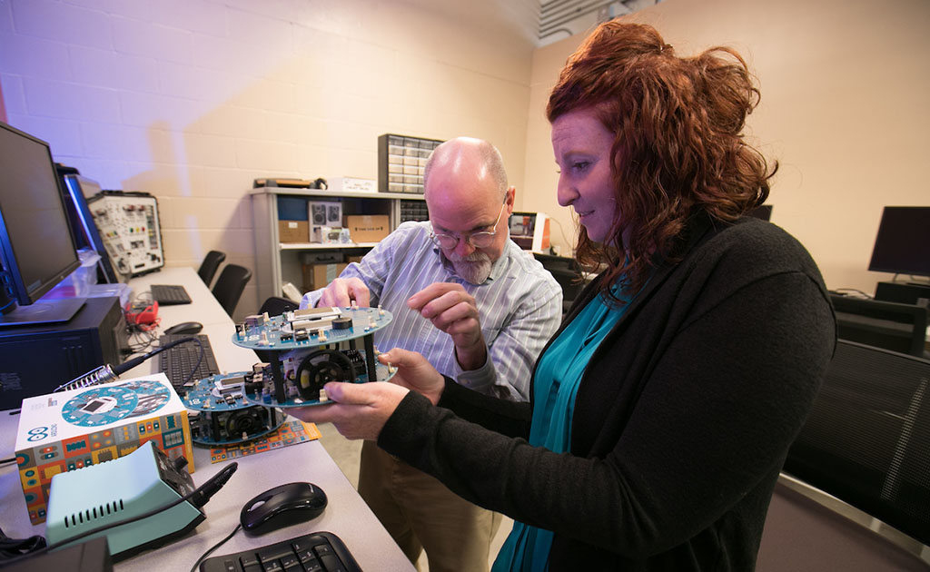 A student receives help with an electronic circuit board from an instructor.