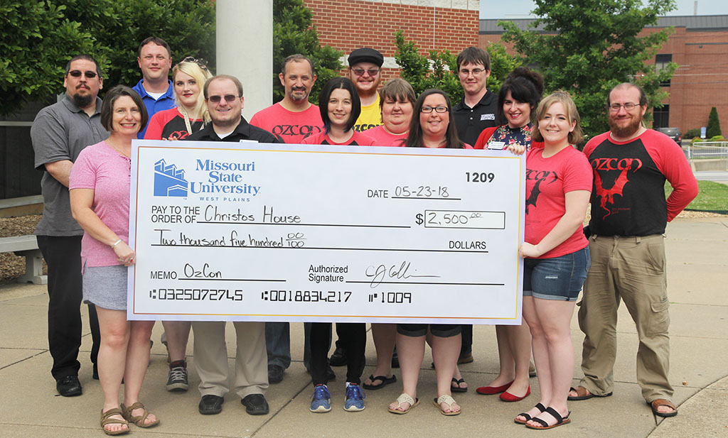 On hand for the check presentation were, front row from left, Christos House Executive Director Moiria Seiber, and OzCon board members Mike Scheidt, Dalyn Bird, Amber Switzer, Meghan Berry, Amber Carr, Breanna Lane and Biff Bird. Back row: Jacob Poulette, CJ Collins, Sarah Corniels, Will Mahan, Jim Listopad and Ben Bird. (Missouri State-West Plains Photo)