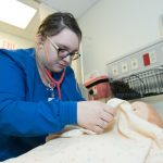 A nursing student uses her stethoscope to listen to the heartbeat of the training mannequin.