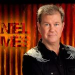 A man standing in front of a red curtain. His name, Daniel James, is written on his left.