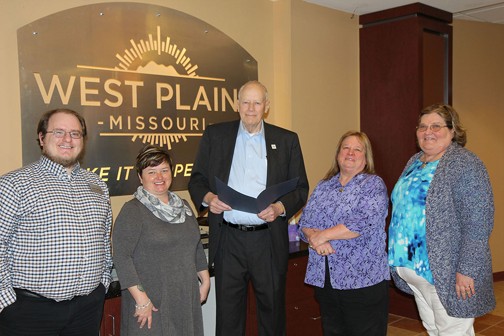 The group is standing in front of the official West Plains city logo at city hall.