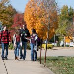 Students walk in a group along a sidewalk outside a classroom building