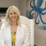 Lynsey Sullivan stands in front of a machine at her workplace. A blue octopus is painted on the wall on the right side of the image.