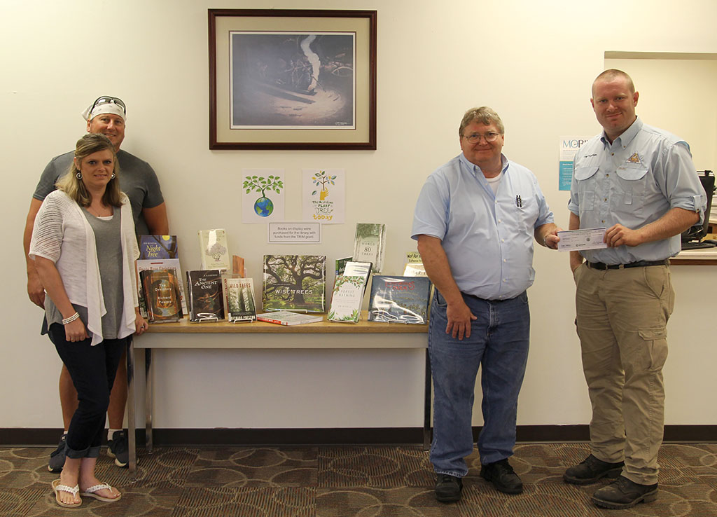 The group stands next to a table in the Garnett Library. On the table are some of the books purchased with TRIM Grant funds.