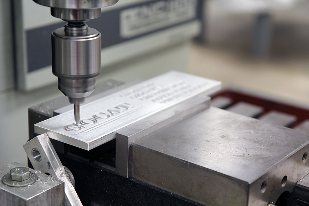 A machine spells out GOCAT on a piece of metal