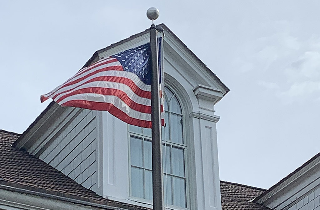 The US flag waves gently in a breeze on a flag pole in front of a building..