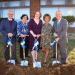 Five people hold shovels preparing to break ground on construction project