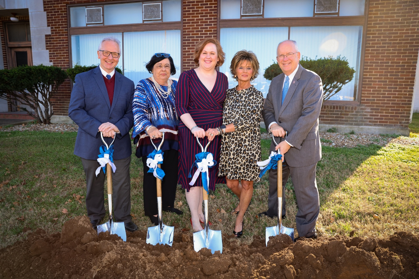 Five people hold shovels preparing to break ground on construction project