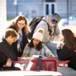Students gathered around an outdoor table looking at a textbook