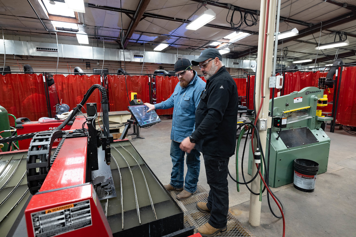 Welding student and instructor program a machine to cut out bear shape from a sheet of steel.