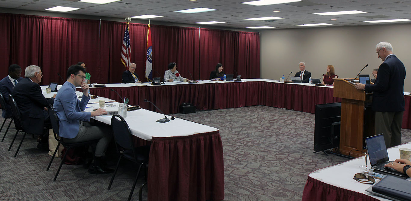 Chancellor Dennis Lancaster stands behind podium at far right. Members of the board are seated around a U-shaped table.