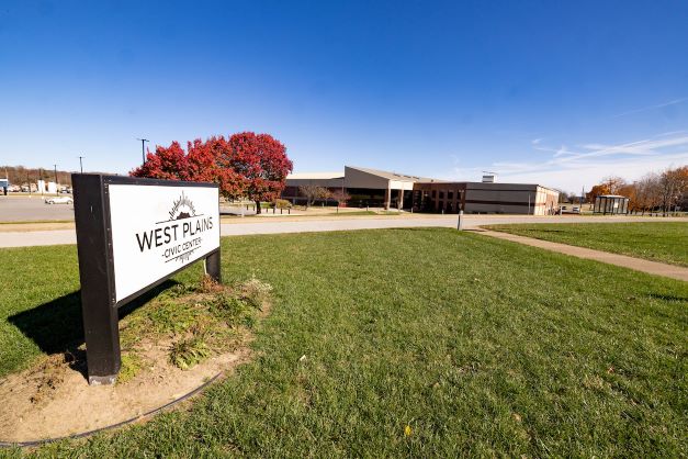 View of the main entrance to the West Plains Civic Center during the fall. The civic center sign is in the foreground at left with a tree with fall leaves and the civic center in the background.