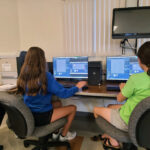 An instructor shows two students how to write programs on their computers.