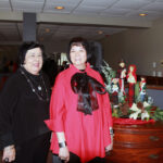 Two women in fine clothing stand in front of table with holiday decorations.