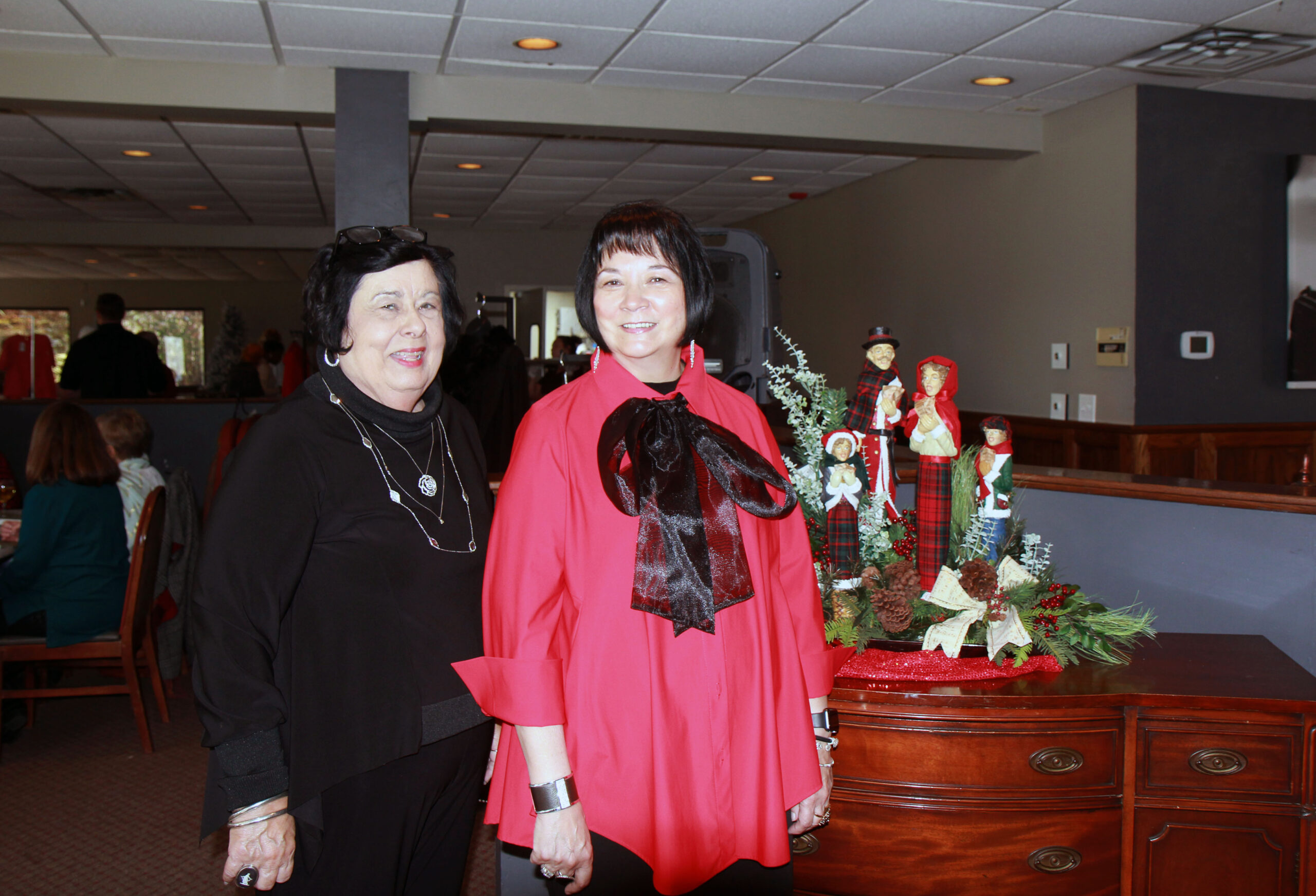Two women in fine clothing stand in front of table with holiday decorations.