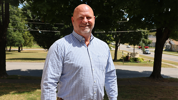 Brian Mitchell poses for a photo in front of shaded trees