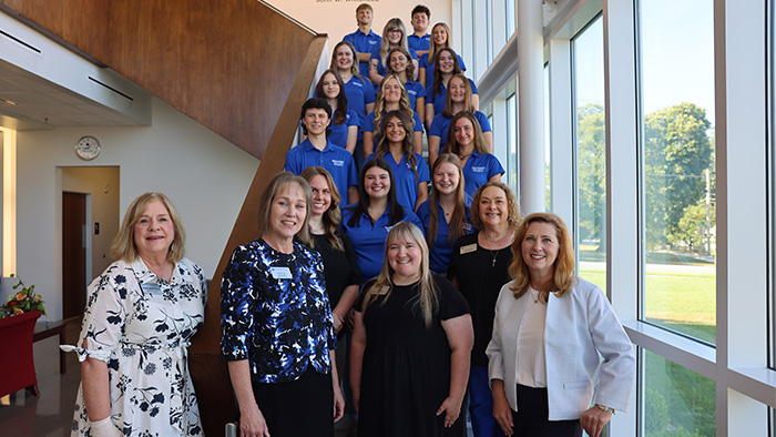 The student ambassadors pose for a group photo wearing blue polos. The admissions staff and Chancellor Zora Mulligan stand in front of them.